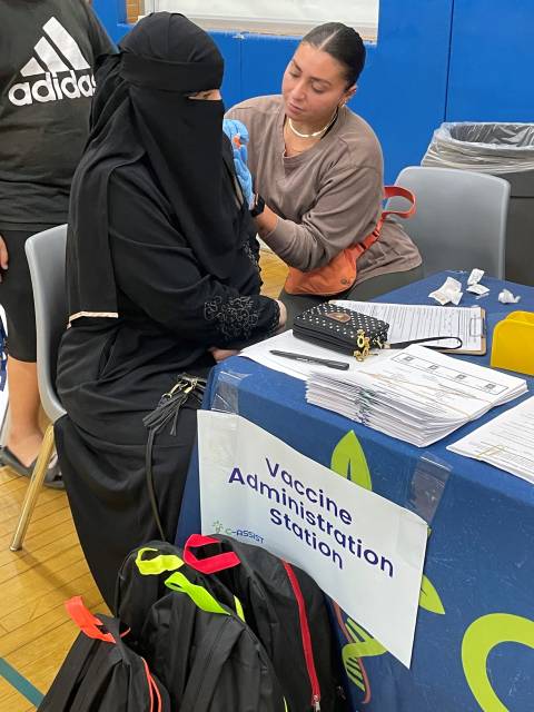 Woman in niqab receiving a flu shot from woman in brown sweater.