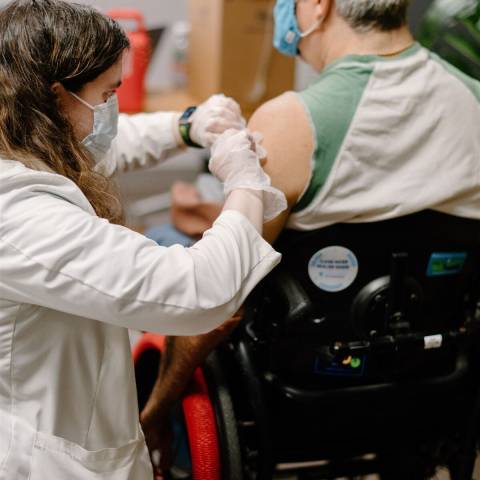 Man in a wheelchair getting a vaccine from a woman in a white coat
