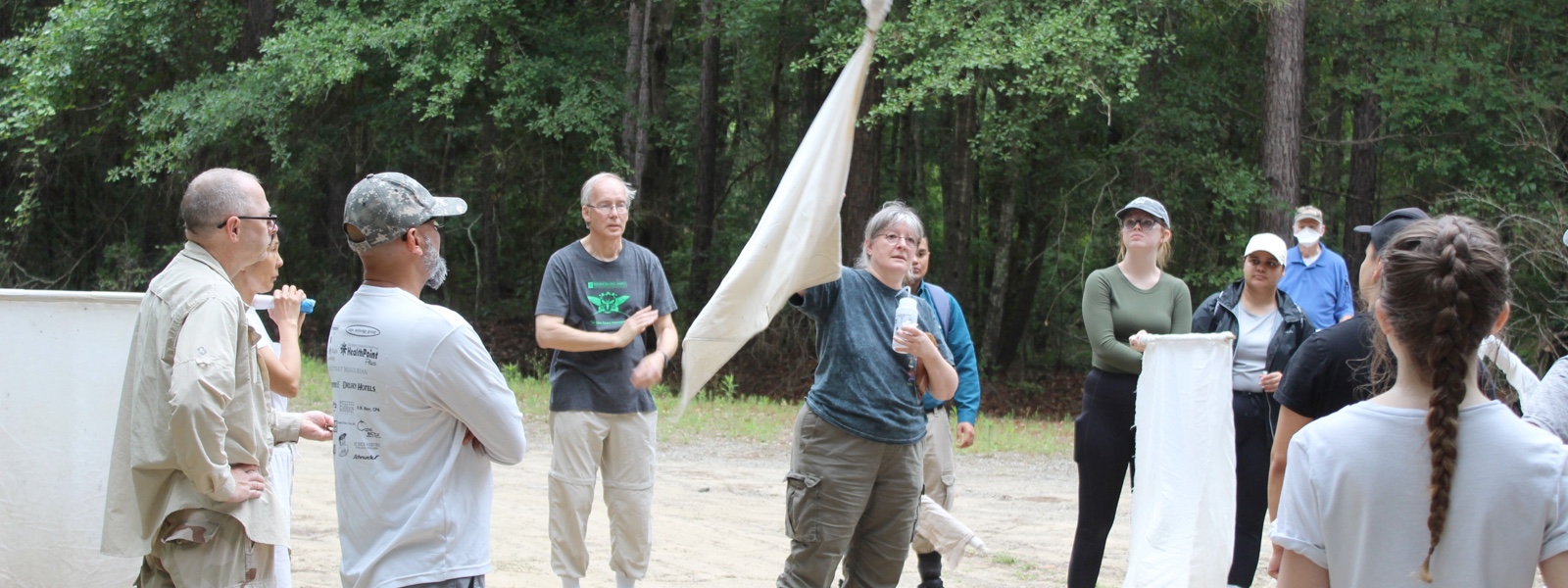 A person holding a piece of tick-collecting fabric giving instructions to a group of people