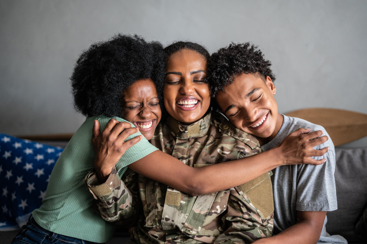 A service member and two other people hugging and smiling