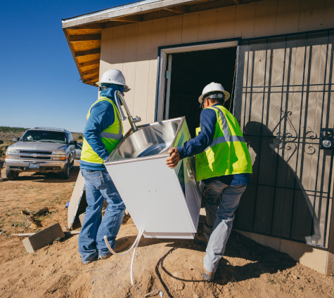 Navajo Water Project staff carry a sink into a household during a home water system installation.