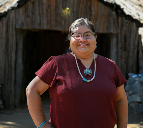 A smiling person standing in front of a wooden building