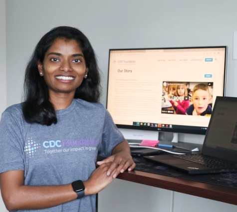 A smiling person seated at a desk. A computer monitor with a CDC foundation website displayed is on the desk.