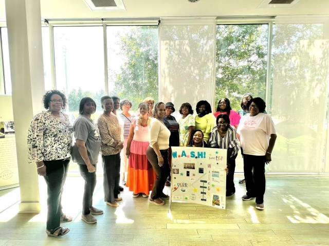 A group of black women pose with a poster that says WATER and SANITATION