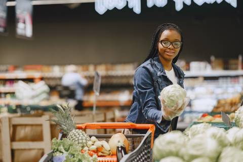 a young Black woman with glasses inspects a head of lettuce at the grocery store