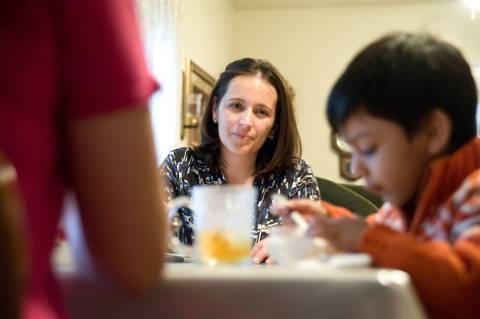 a mother watches over her son as they eat together at the kitchen table