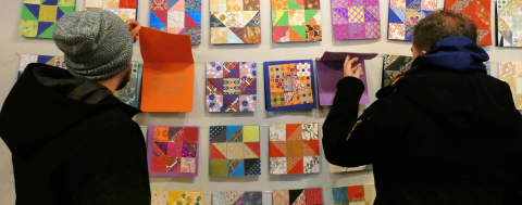 two visitors look closely at individual "barn quilt" designs with messages written inside