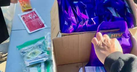 A hand reaches for a purple bag with HIV self-testing information