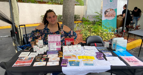 A person in a floral top sits at a table filled with HIV self-testing pamphlets and kits