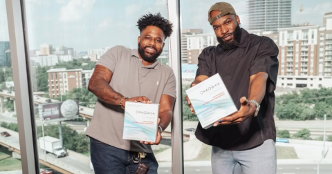 Two men hold HIV self-testing kits in front of a window overlooking a city.