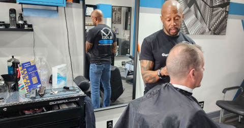 A man cuts another man's hair in a barbershop. HIV self-testing materials are displayed on the counter.