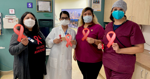 Four people in scrubs and face masks hold up red HIV/AIDS awareness ribbons.