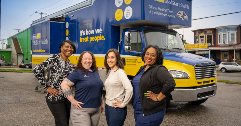 Four women pose in front of a large navy truck that says "MedStar Health"