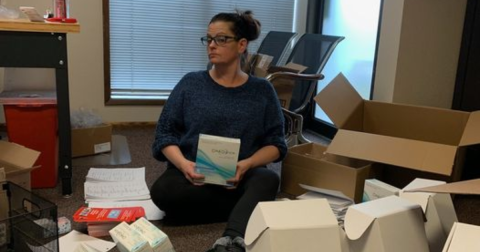 A woman sits in front of empty boxes holding an HIV self-testing kit.