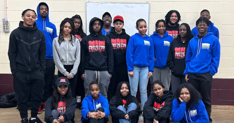 A group of African American teens post for a camera wearing blue and black sweatshirts