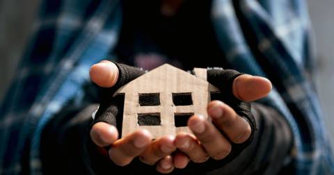 Close up of hands with fingerless gloves holding a cardboard cut out of a house