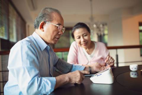 An older Asian couple looks at a blood pressure readout.